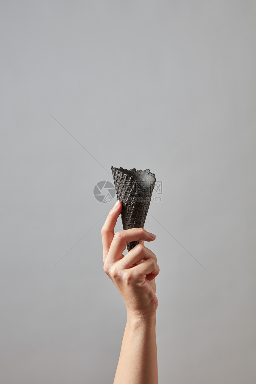 个女人的手着个清脆的空黑华夫饼锥深灰色的背景上,为您的商业想法提供新鲜的空黑华夫饼锥女手灰色背景与图片
