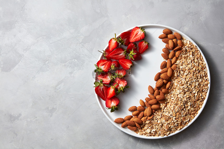 成熟的草莓,杏仁燕麦片个盘子上的灰色混凝土背景与,顶部视图饮食健康饮食盘子与生燕麦片,坚果草莓灰色混凝图片