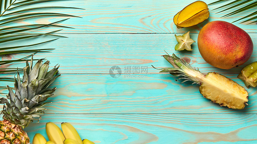 棕榈树的绿色枝条套同的热带水果蓝色的木制背景上,文字的食物架平躺食物框架来自同的热带水果棕榈枝蓝图片