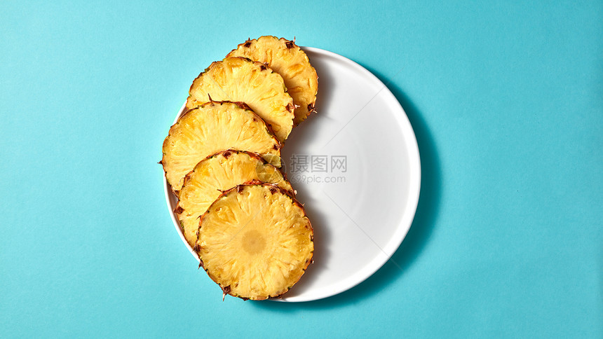 切片菠萝个白色的盘子,食物成蓝色的纸背景与,顶部视图开胃的菠萝片个白色的盘子蓝色的纸背景顶部的视图图片