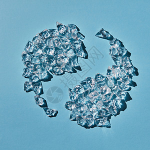 阴阳符号的形状由蓝色背景上阴影的透明人造冰块成的顶部视图蓝色背景上以阴阳符号的形式的碎冰块的风景背景图片