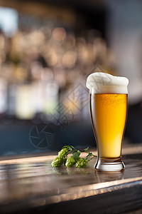 酒吧酒吧桌上的冷啤酒杯啤酒花锥的木制桌子上的杯啤酒模糊的背景图片