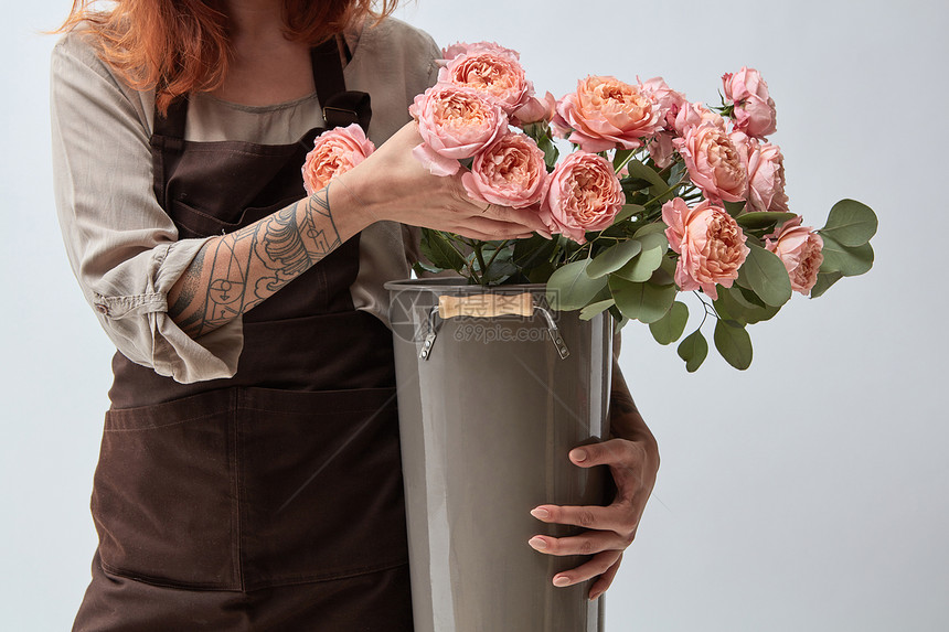 个穿着棕色围裙的女人着个花瓶,新鲜的粉红色玫瑰花店的粉红色的玫瑰穿着围裙的女孩手里图片