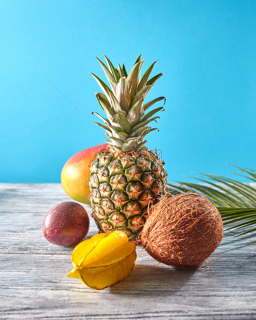 夏季构图与健康的异国水果新鲜菠萝,杨桃,西番莲,椰子,芒果棕榈叶灰色木桌上的蓝色,健康饮食的异国水果热图片