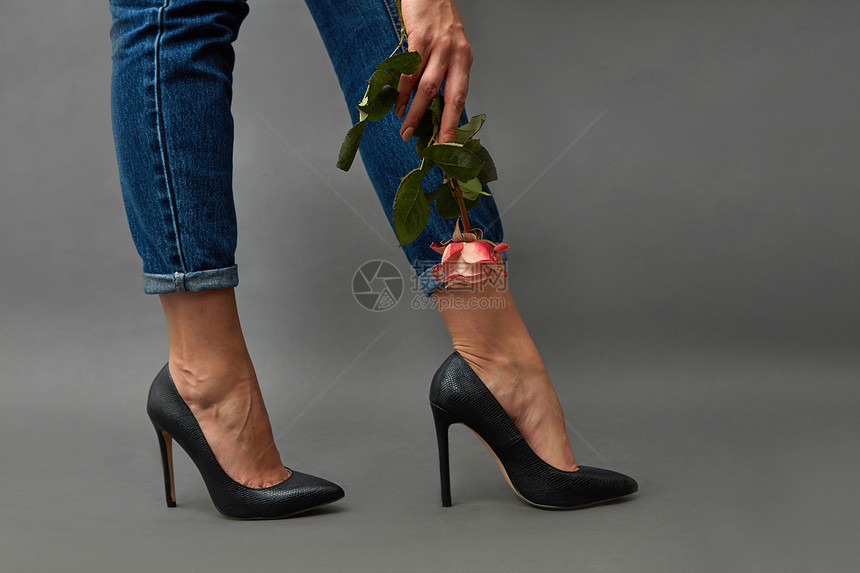 优雅的女孩腿穿着牛仔裤高跟鞋,个纹身的女孩的手着朵粉红色的花,围绕着个黑色的背景漂亮的女腿穿着黑色的鞋图片