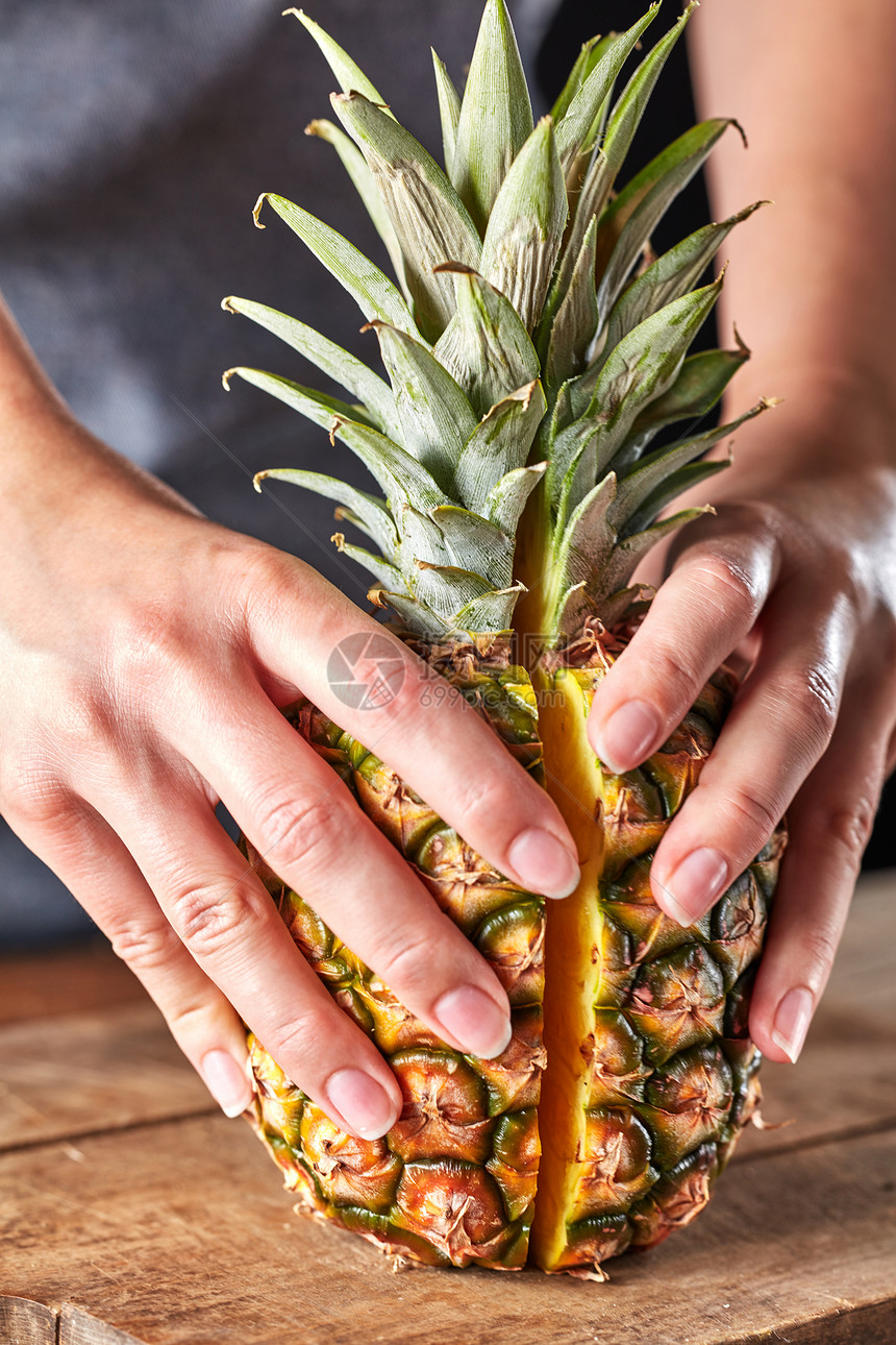 女人的手着菠萝两半,绿叶放木制厨房桌子上健康产品新鲜的半片异国菠萝把女孩的手放木制厨房板上维生素水果图片