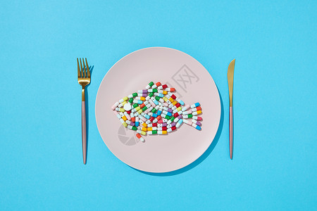 欧米茄6许多同的药丸补充剂食物圆形白色盘子与叉子刀减肥药补充剂的饮食顶部视图彩色胶囊药丸,以鱼的形式盘子背景