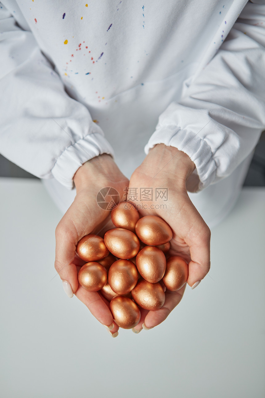 女人的手着灰色背景周围的彩绘金色的小鸡蛋财富的风景金色的小鸡蛋握着灰色背景上女人的手图片