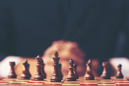 商人的老式风格形象,双手紧握,规划策略,张旧木桌上摆着国际象棋人物图片