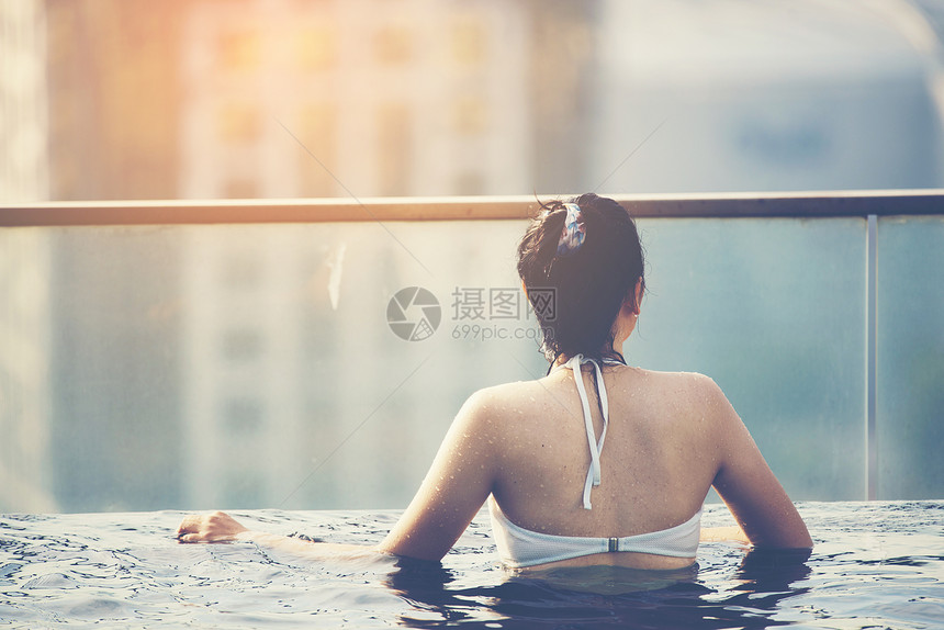 轻女子屋顶游泳池与美丽的城市景观,阳光老式过滤图像图片
