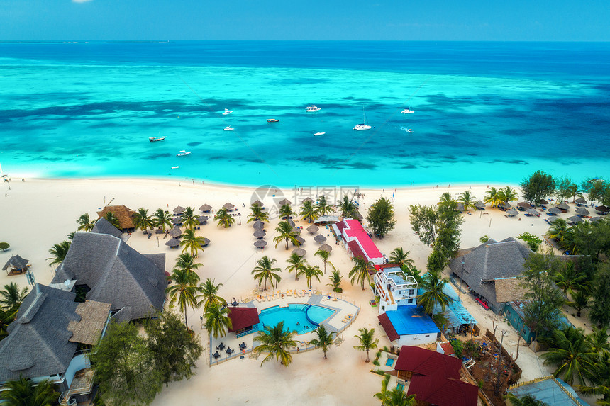 阳光明媚的日子里,用手掌雨伞俯瞰热带沙滩印度洋,桑给巴尔,非洲的暑假景观棕榈树,酒店,游泳池,白沙,蔚蓝的大海图片
