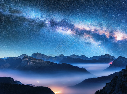多彩星空光效夏天的夜晚,雾中的山上银河景观与高山山谷,低云,紫色星空与银河,城市照明空中飞行帕索Giau,白云石,意大利背景