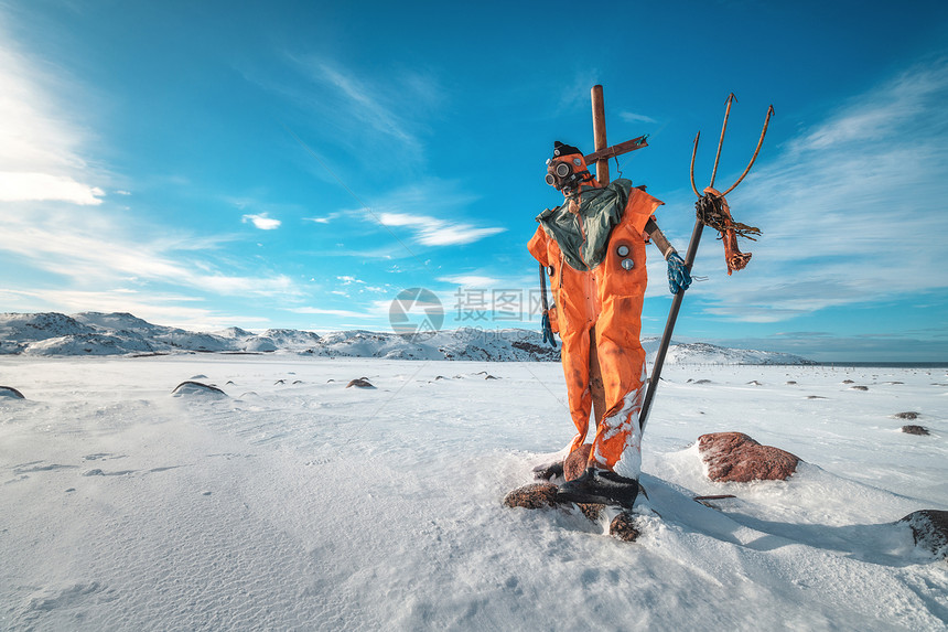 稻草人穿着橙色的衣服,戴着三叉戟的防具,着蓝天,云彩雪域冬季景观与趣的假人,石头雪山脉泰伯卡,俄罗斯旅行图片