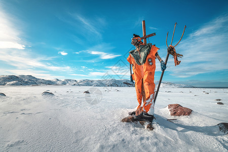 稻草人穿着橙色的衣服,戴着三叉戟的防具,着蓝天,云彩雪域冬季景观与趣的假人,石头雪山脉泰伯卡,俄罗斯旅行背景图片