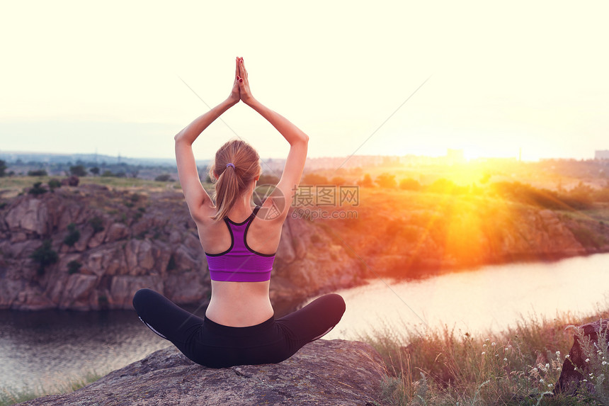 轻的女人河边日落时山上练瑜伽图片
