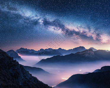 多彩星空光效夏天的夜晚,银河雾中飞过群山景观雾的高山山谷,紫色的低云,五颜六色的银河星空,城市照明意大利白云石背景