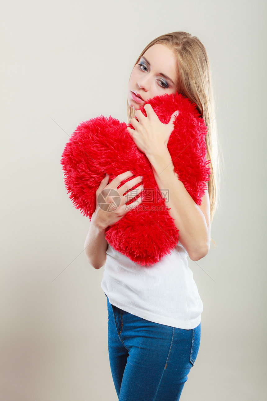 破碎的心的爱的悲伤幸的女人抱着红心枕头图片