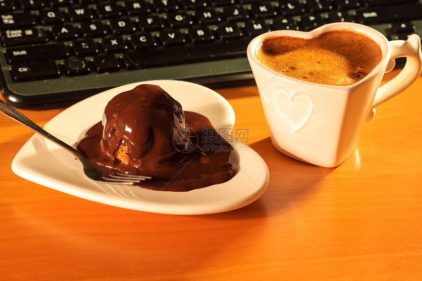杯咖啡巧克力蛋糕心形盘子碟子旁边的笔记本电脑键盘办公室办公桌电脑旁边的杯咖啡巧克力蛋糕图片