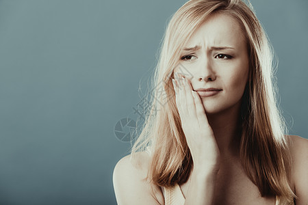 牙科护理牙痛特写轻女子脸担心女孩患牙痛,灰蓝色墙壁背景图片