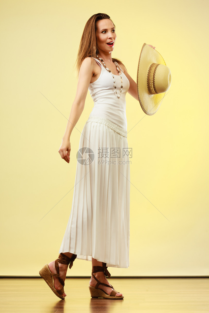 假日夏季时尚女人戴着大草帽白色连衣裙女模特明亮的黄色背景上展示全长图片