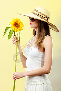 迷人的夏天女人戴着太阳镜,草帽,手里着黄色背景的向日葵背景图片