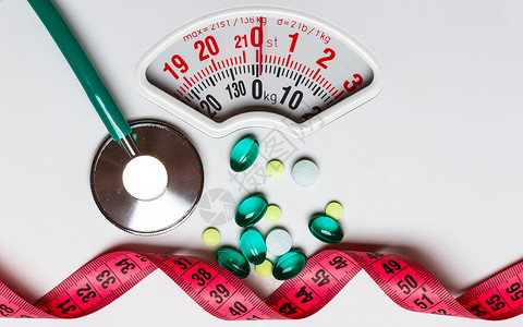 重量仪器健康饮食医药保健食品补充剂减肥理念带测量带听诊器的药丸白色鳞片上背景