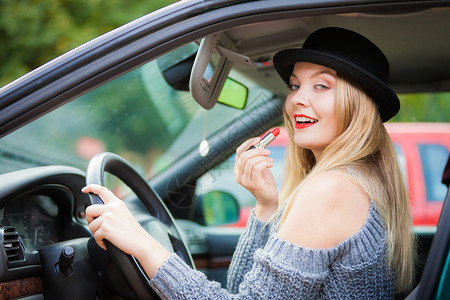 轻迷人的女人看着后视镜,画着她的嘴唇,开车时化妆轻的女人车里涂口红图片