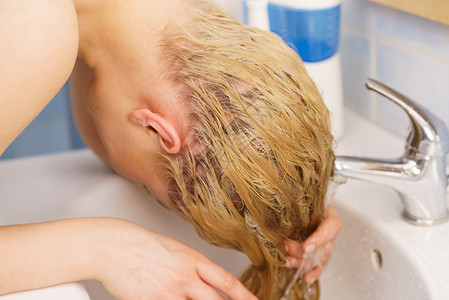 女人浴室水槽里洗她长长的金发家理发的女人浴室水槽里洗头发图片