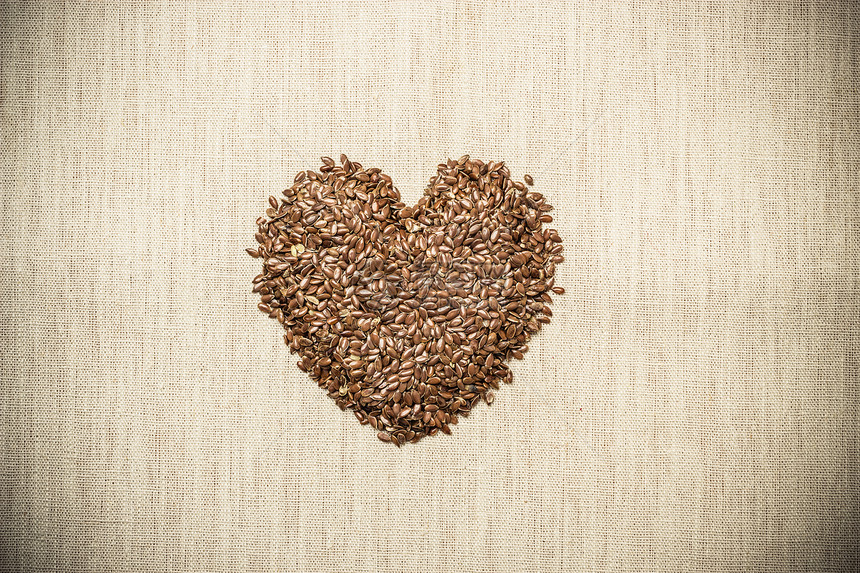 饮食保健健康食品生亚麻籽亚麻籽心形状的麻袋麻布背景图片