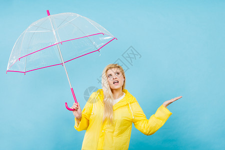 金发女人戴着黄色雨衣,着透明的雨伞检查天气,如果下雨的话图片