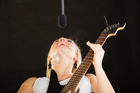 音乐,歌唱音乐天赋的女人电吉他上演奏,演播室唱歌,黑色背景女人弹电吉他唱歌图片