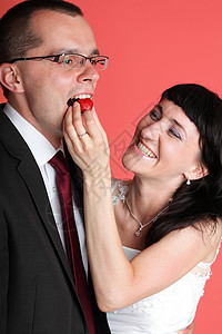 幸福微笑的新娘新郎轻的幸福夫妇玩味地吃着红色背景上的稻草背景