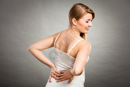 长时间的工作时间健康背痛的轻女患背部疼痛的女人灰色患背痛的女人图片