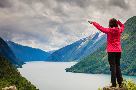 土地税旅行游客女人用手指看着挪威峡湾美丽的山脉景观挪威山脉峡湾的女游客背景