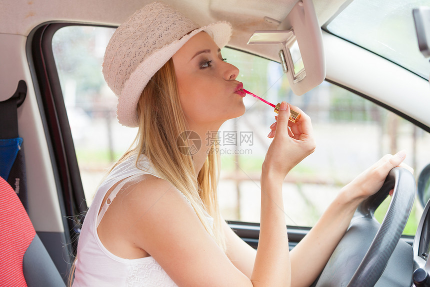 分心的司机轻迷人的女人看着后视镜,画着她的嘴唇,开车时化妆开车时化妆的女人图片