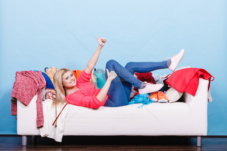 服装困境的快乐的懒女人躺凌乱的沙发上,穿着成堆的衣服快乐的女人躺凌乱的沙发上图片