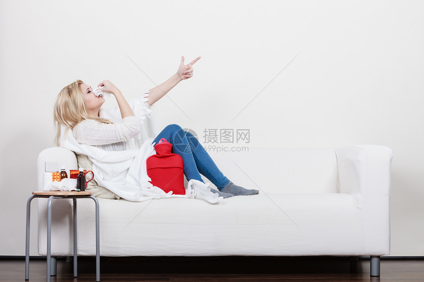 疾病,季节病问题的患流感的女人躺沙发上打喷嚏,用纸巾指着电脑躺沙发上患流感的女人生病了图片