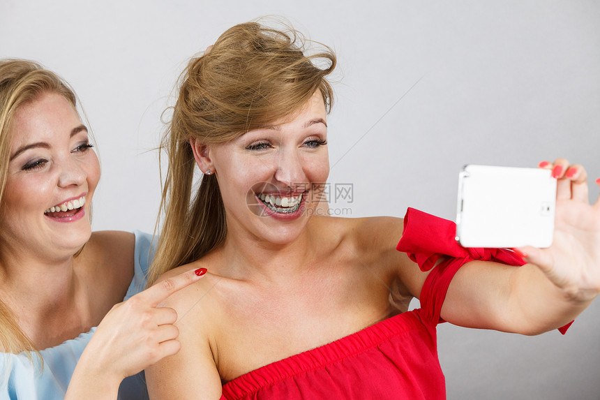 时尚的两个女人用智能手机自拍,玩得开心,享受朋友的时间时尚的女人自拍图片