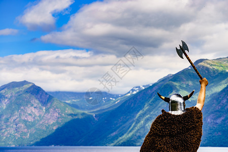 威武男战士挪威峡湾岸边戴着头盔斧头的维京战士旅游旅游挪威峡湾海岸的维京战士背景