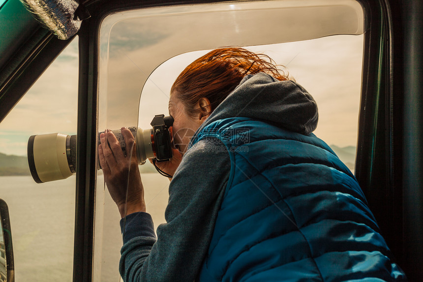 成熟的女旅游专业摄影师用相机露营车上拍照,开车上路女乘客窗外拍照,刮风的天气摄影师露营车里拍照图片