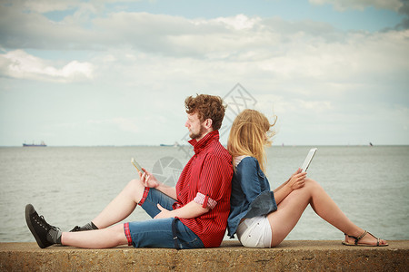 现代技术设备轻夫妇户外抗天空男人与智能手机,女人与平板电脑享受暑假图片