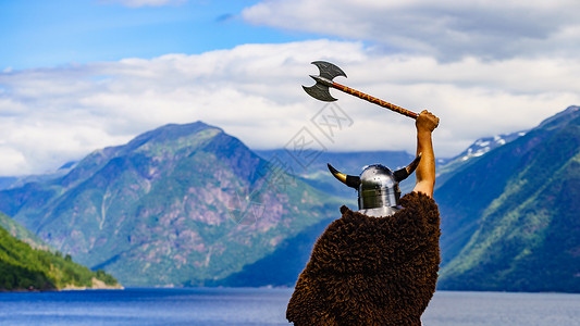 威武男战士挪威峡湾岸边戴着头盔斧头的维京战士旅游旅游挪威峡湾海岸的维京战士背景
