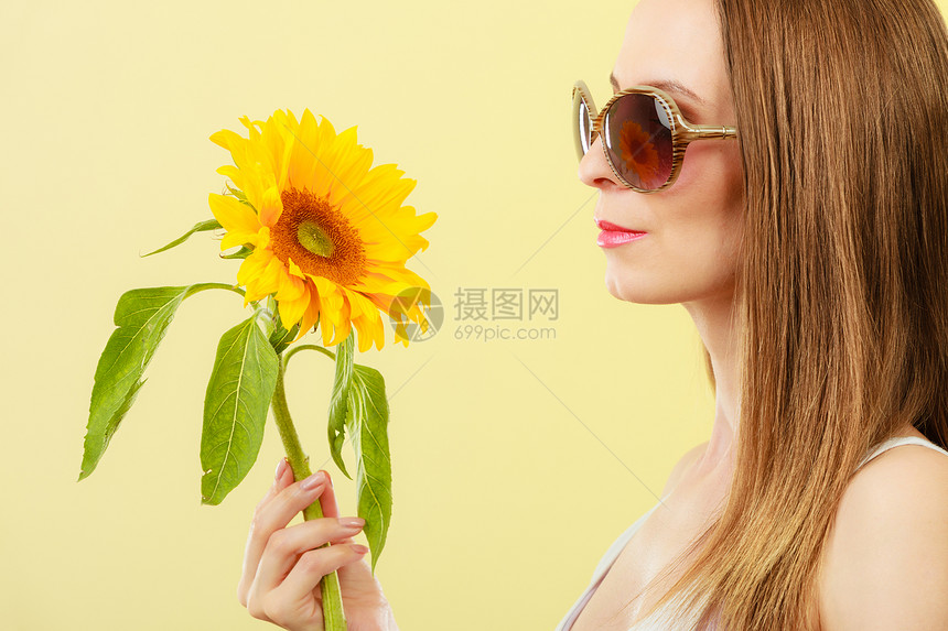 特写侧视迷人的夏季妇女戴着太阳镜,手里着黄色背景的向日葵图片