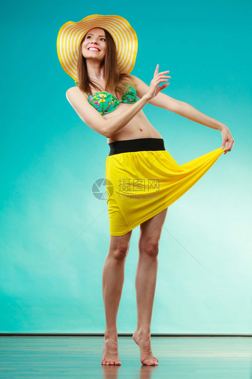 假日夏季时尚戴着黄色帽子比基尼的女人女模特蓝色背景上展示全长图片