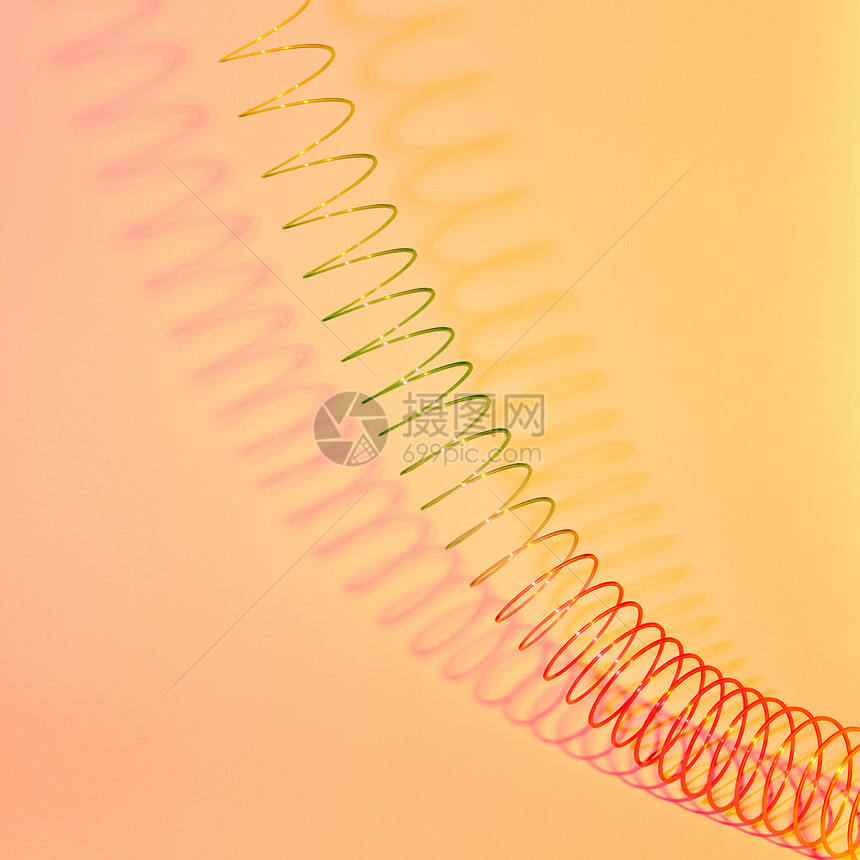 双曲线的几何形状,拉伸彩色塑料螺旋柔阴影的柔黄色背景上,拉伸彩虹塑料弹簧玩具与阴影图片