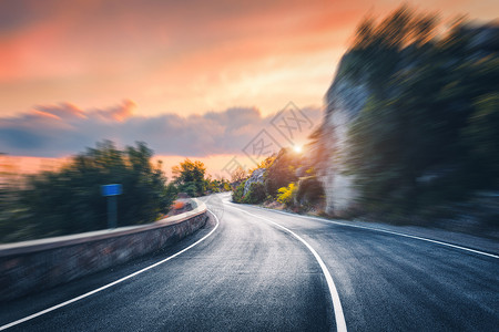 日落时的山路运动模糊的效果沥青路模糊的背景与岩石,橙色阳光明媚的天空与云夏天快速驾驶美丽的公路运动中运背景图片