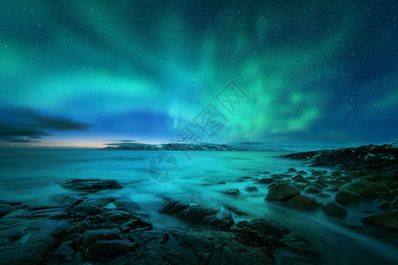 特里伯克北极光岩石海滩海洋上俄罗斯泰伯卡的北极光极地灯光的星空夜间冬季景观与极光,大海与石头模糊的水,雪山背景