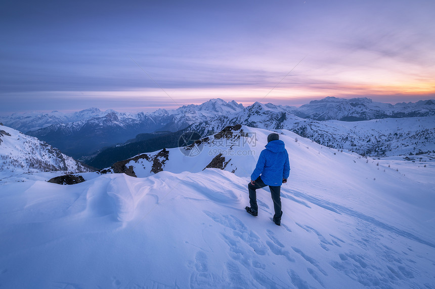 冬天日落时雪山上的轻人山顶上的运动人,黄昏时白雪覆盖的岩石五颜六色的蓝天上云白云岩中旅行与游客欣赏风景图片