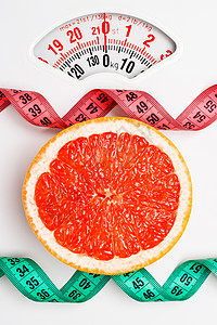 节食健康饮食减肥理念用白色重量秤上的测量带特写葡萄柚切片图片
