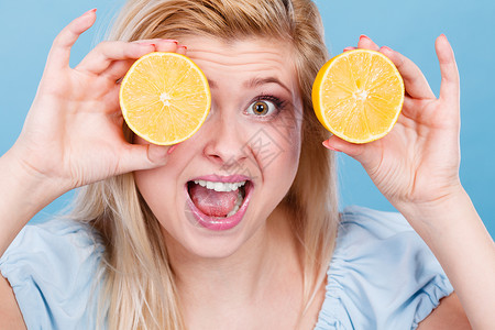 好汉两个半女人十几岁的女孩手里着两个半黄色柠檬柑橘类水果,遮住了眼睛,蓝色的健康的饮食营养快乐趣的女孩用柠檬柑橘类水果遮背景